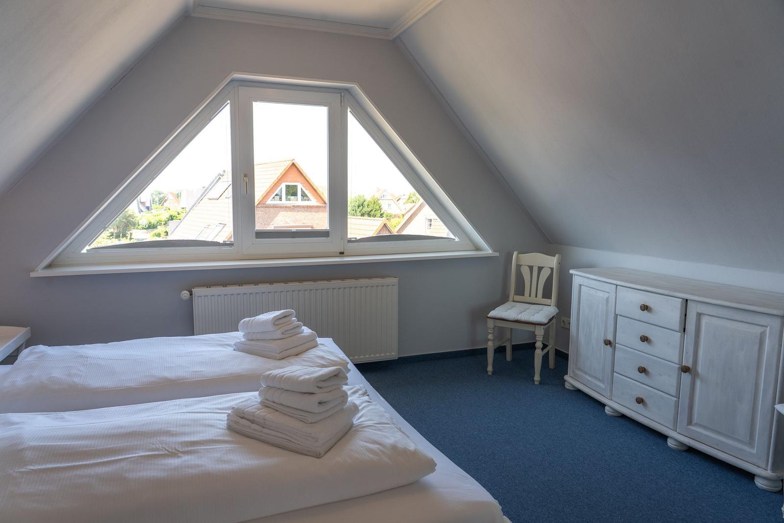 Schlafzimmer mit Dachschrägen, Fenster und Bett mit Handtüchern.