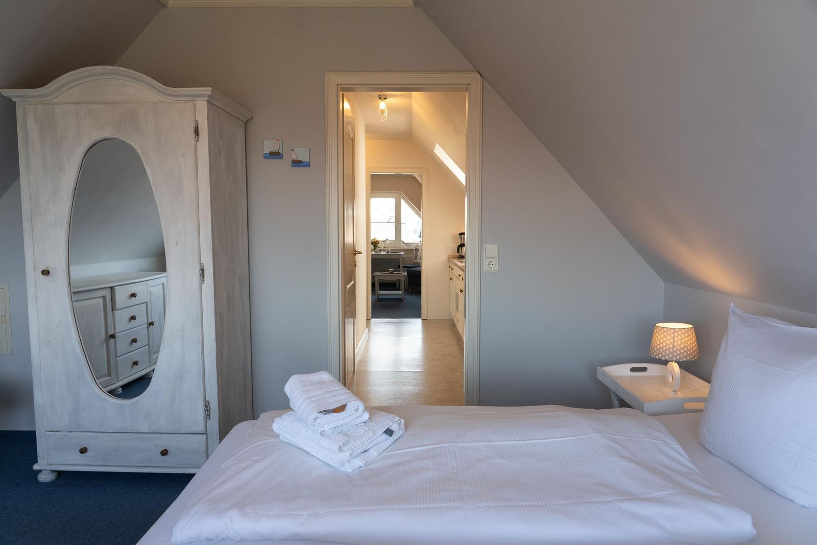 Schlafzimmer mit Dachschräge, weißem Bett und Kleiderschrank mit Spiegel.