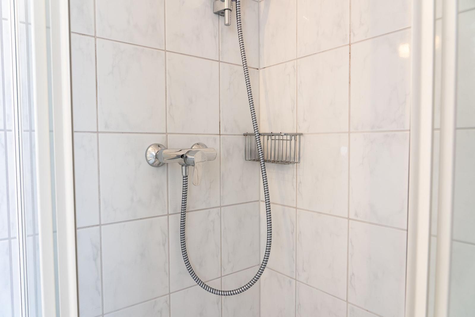 Dusche mit Handbrause und Duschgitter an weißen Fliesen