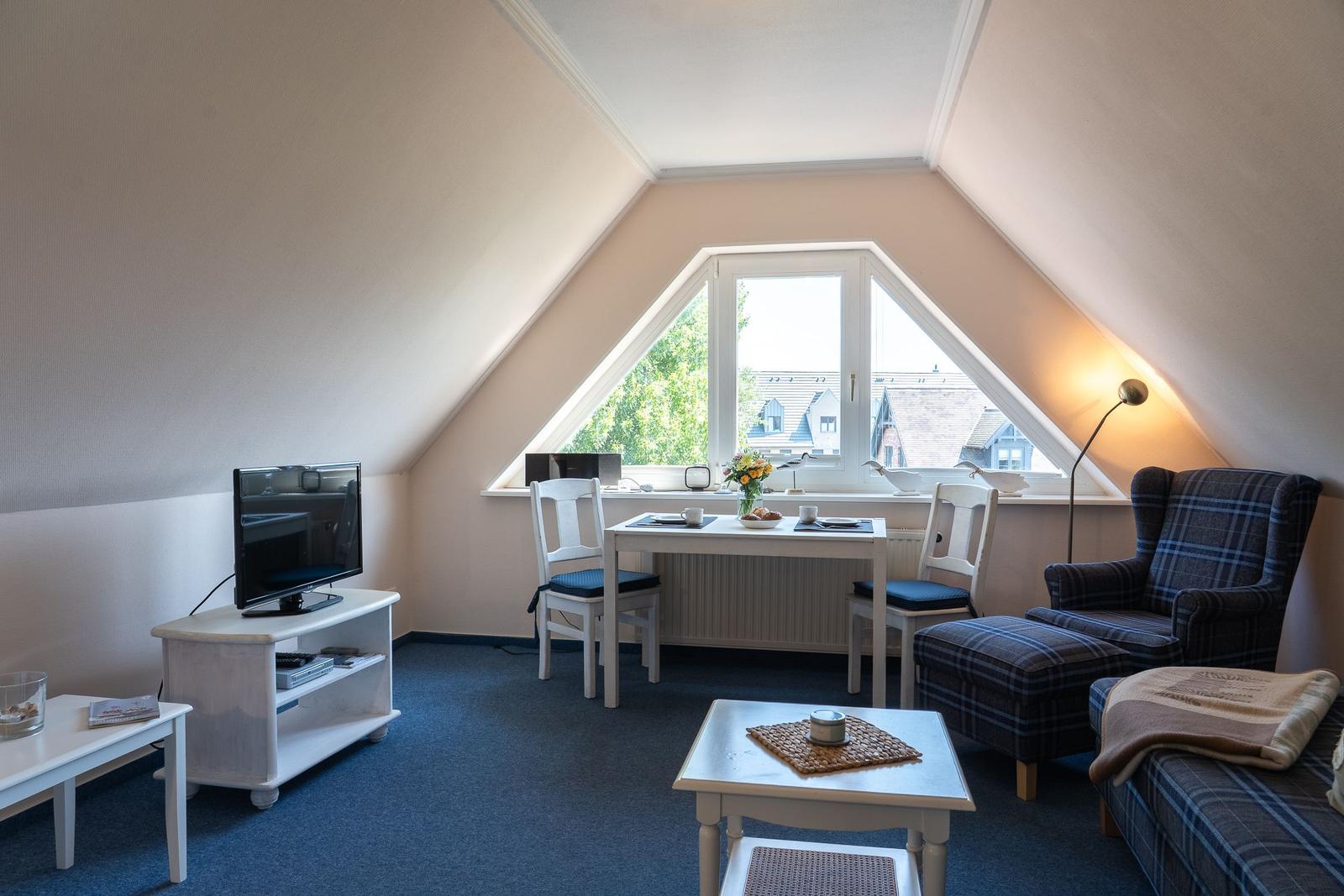 Zimmer mit Dachfenster, Tisch, Stühlen, Fernseher und Sitzgelegenheiten.