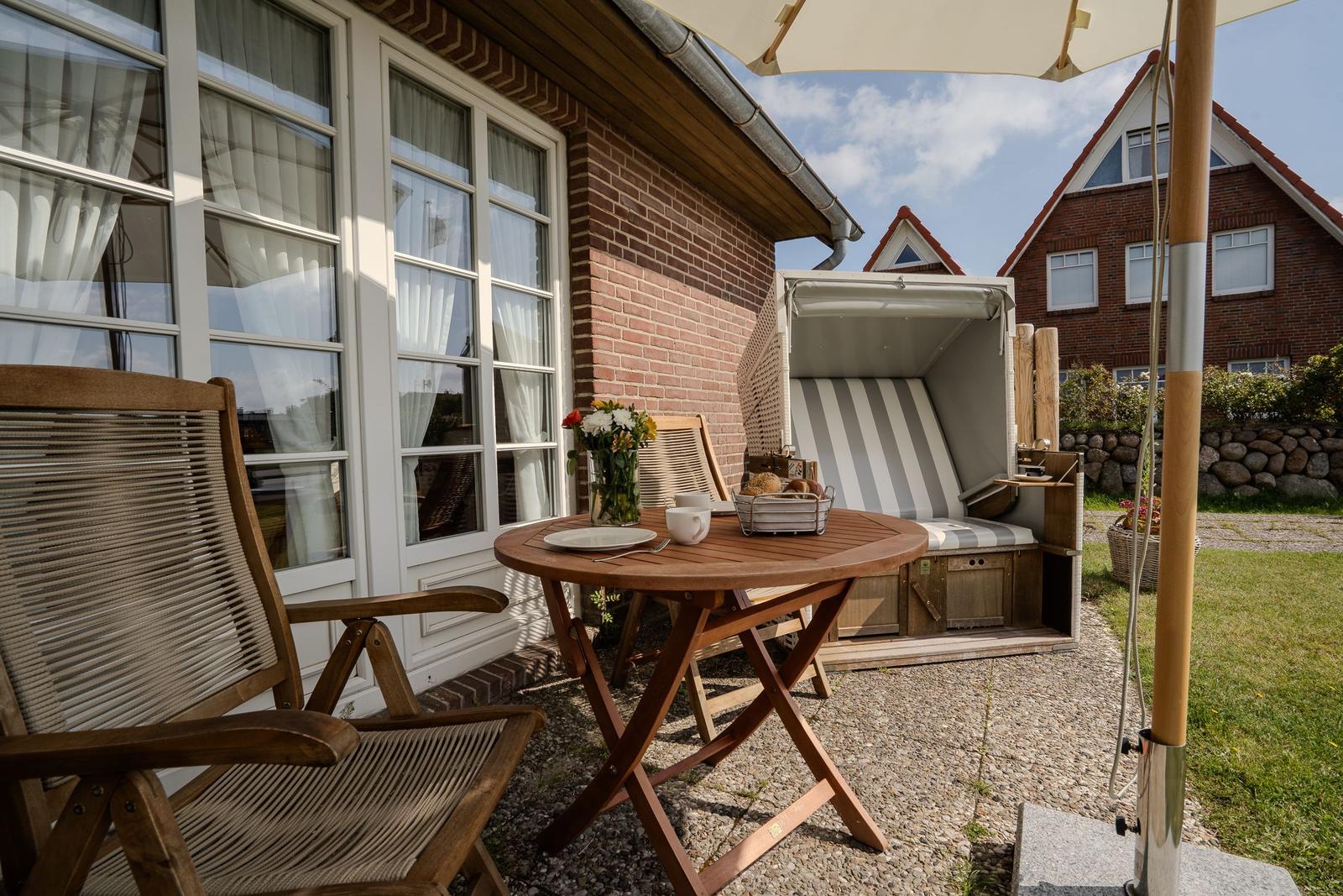 Terrace with table, chairs, and beach chair. Background: house with windows and garden.