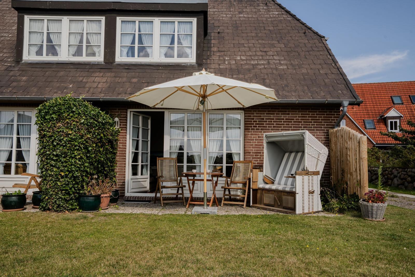 House with garden, umbrella, loungers, and flowerbeds.