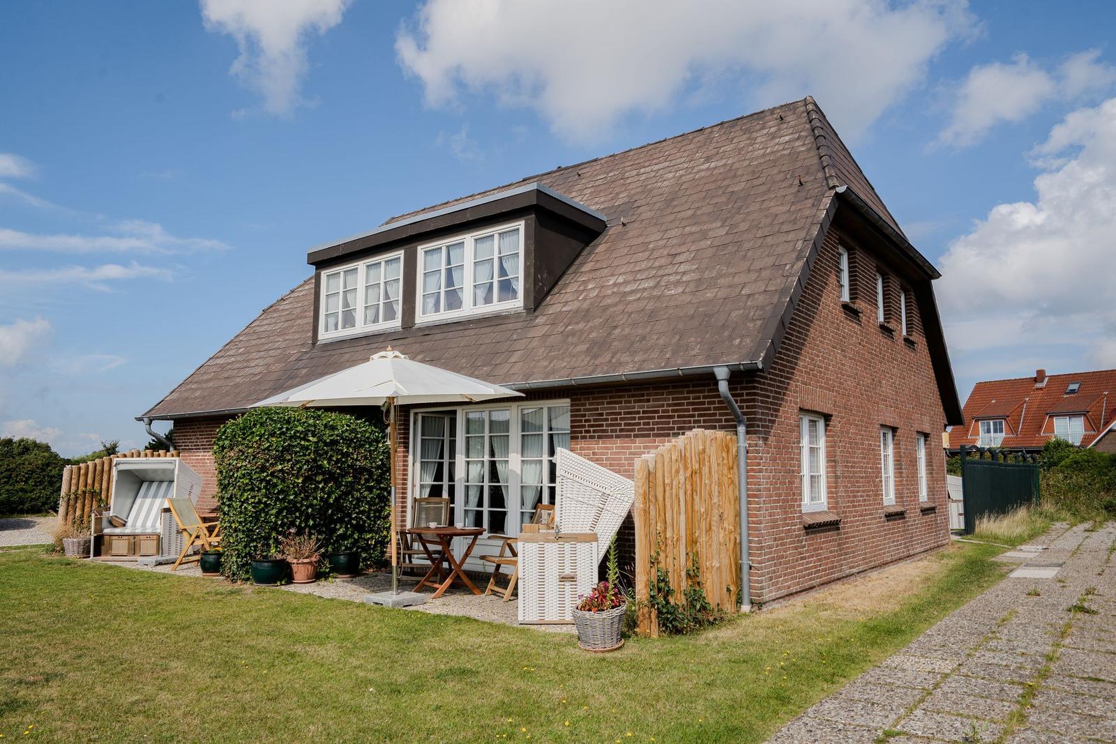 Red brick house with terrace and garden. White windows and sliding doors.