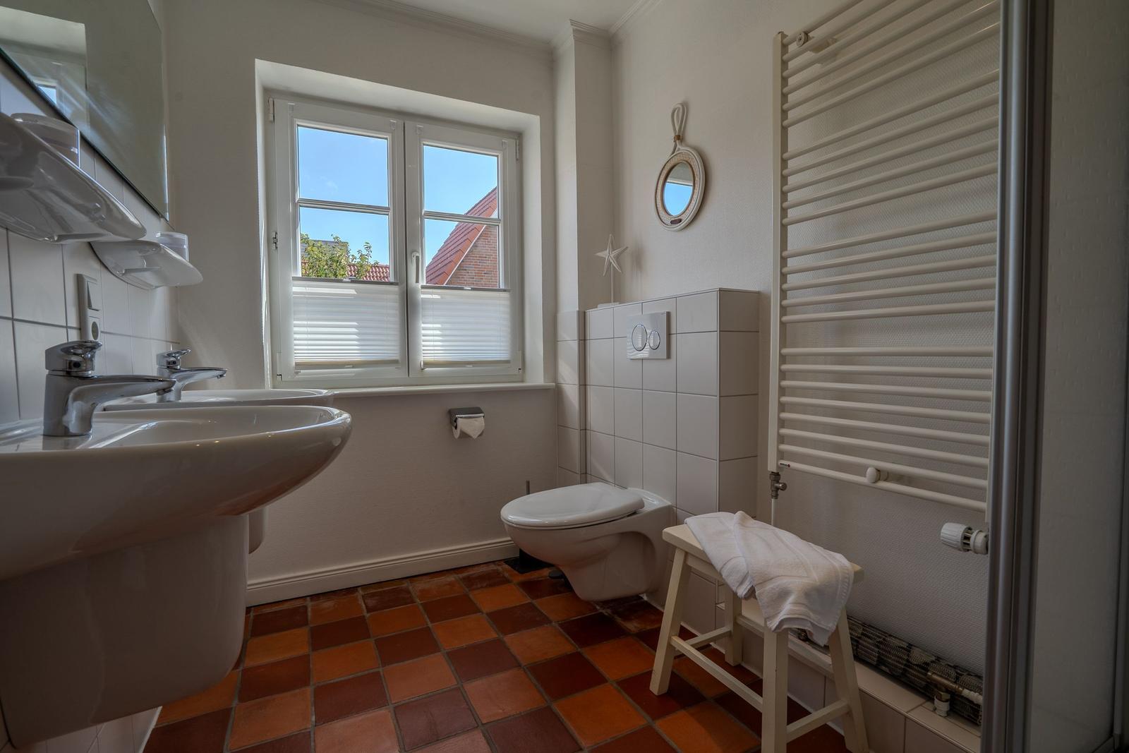 Bathroom with sink, toilet, and window. Terracotta floor and radiator.