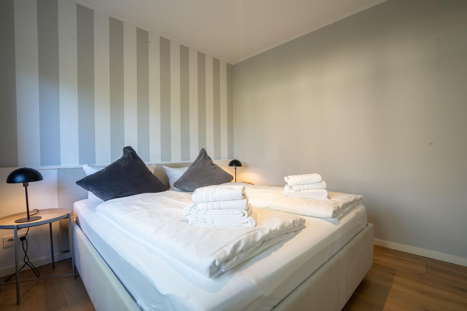 Schlafzimmer mit Bett, Kissen und Handtüchern. Wand mit Streifenmuster.