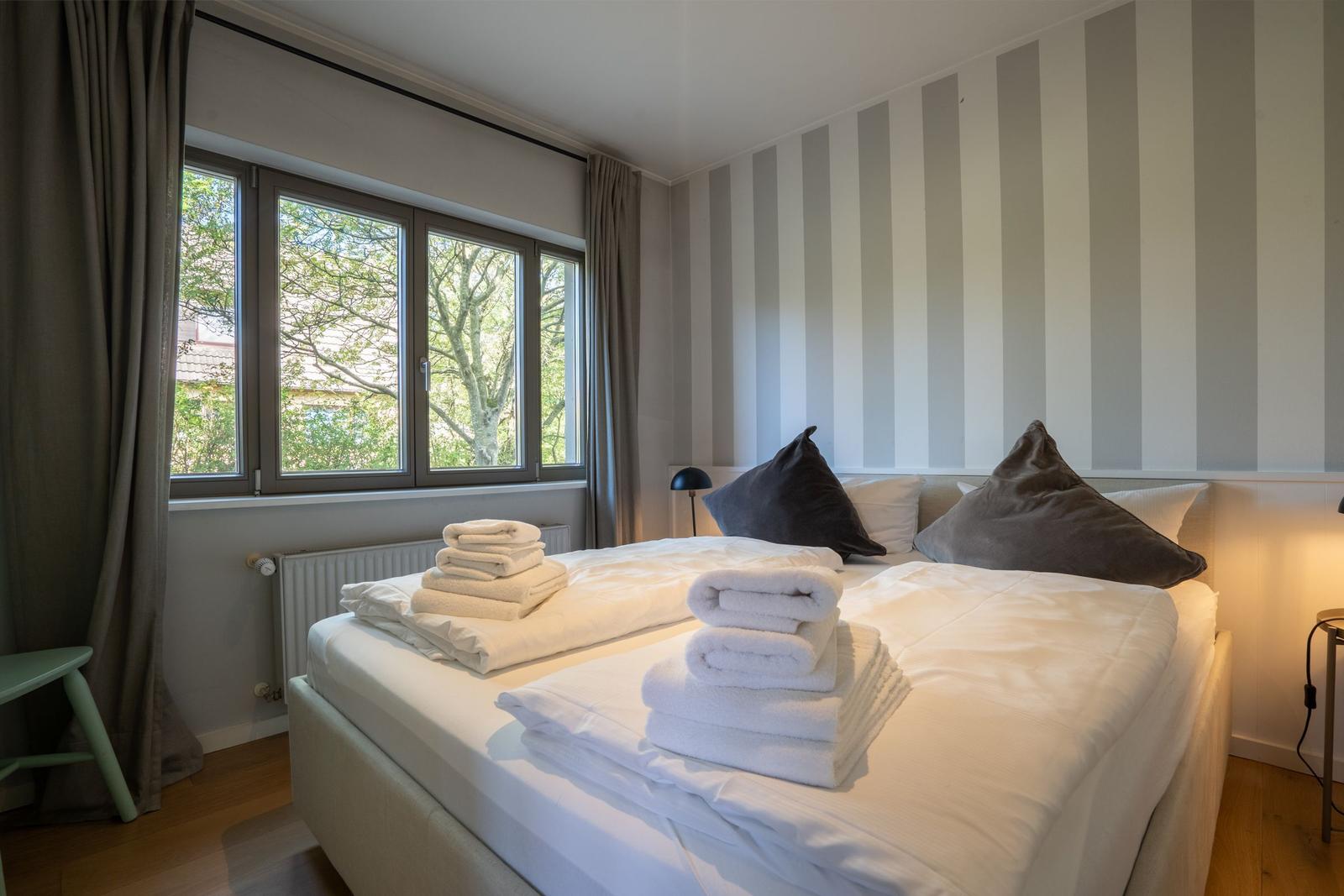 Schlafzimmer mit Bett, Fenster und gestreifter Wand