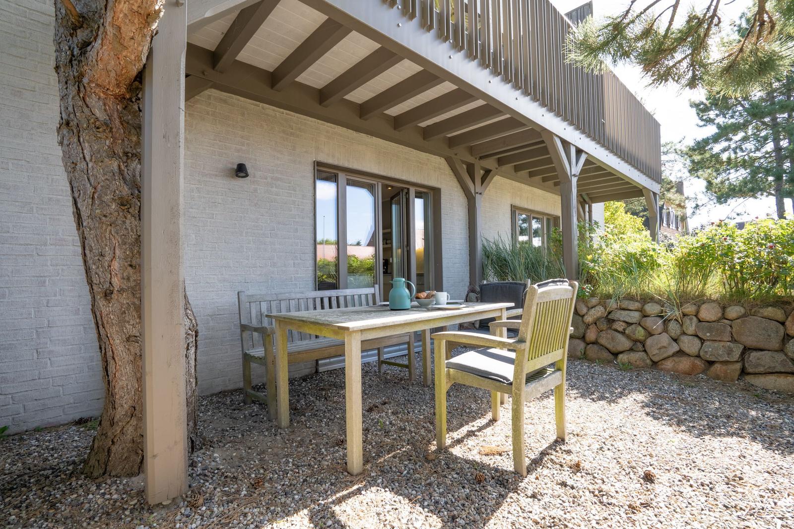 Terrasse mit Tisch, Stühlen und Blick auf Balkon und Garten.