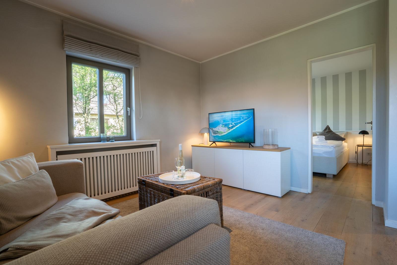 Wohnzimmer mit Sofa, Fernseher und Blick auf Schlafzimmer.