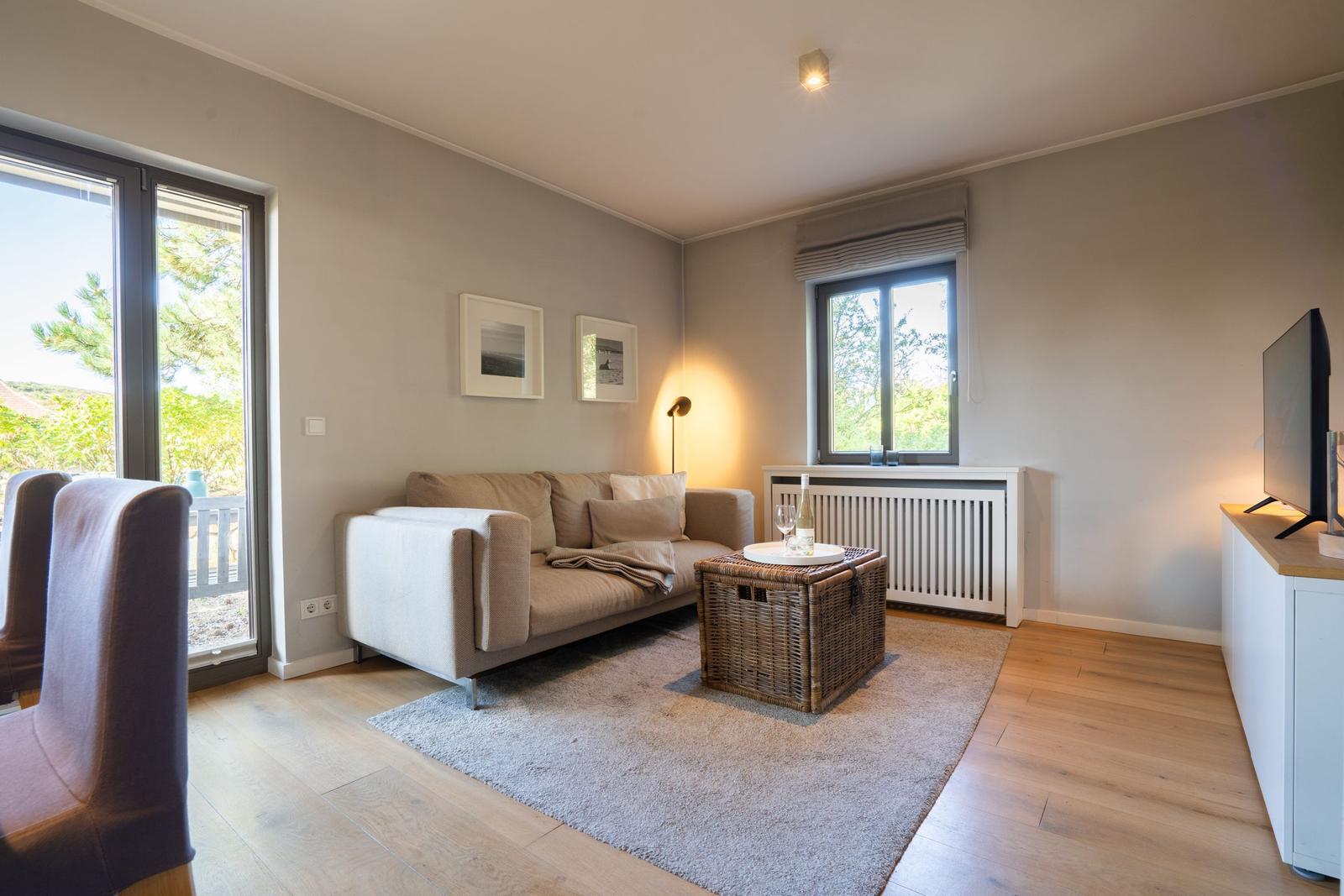 Wohnzimmer mit Sofa, Korbtablett und TV. Durchgangstür zum Balkon.