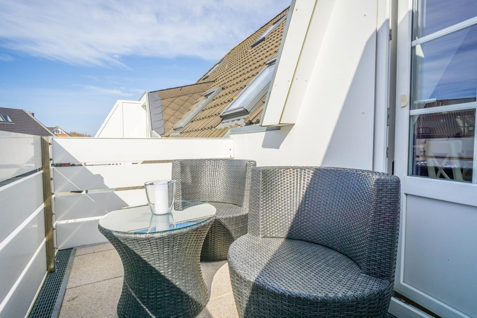 Terrace with two chairs and table. Background: roof with skylights.