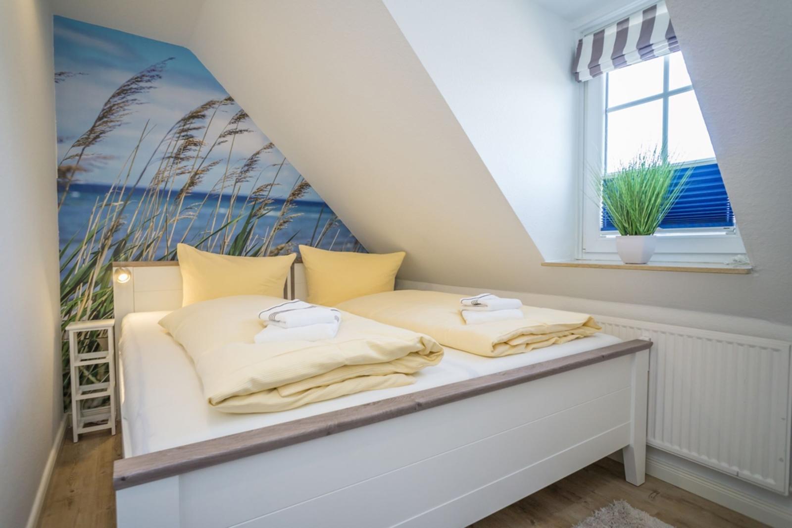Bedroom with sloped ceiling, bed with yellow pillows, and wall mural of beach.