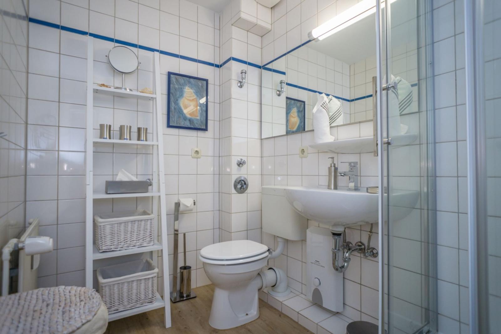 Bathroom with shower, sink, and toilet. White tiles and blue accents.