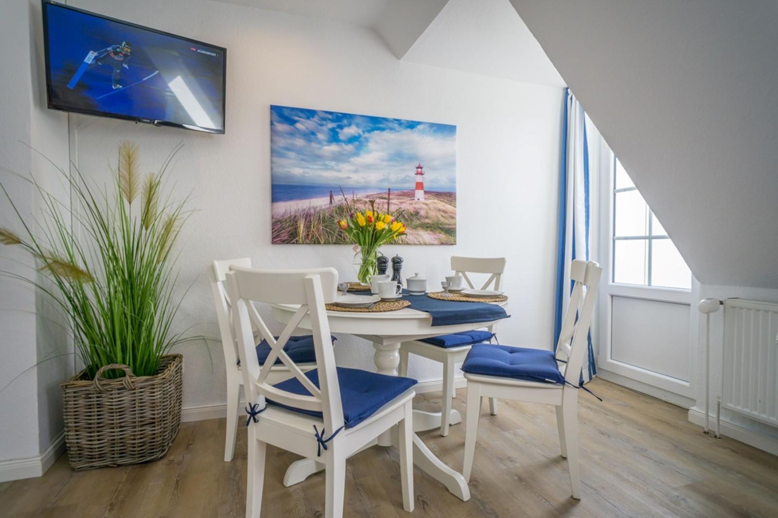 Dining room with white table, blue seat cushions, and lighthouse wall art.