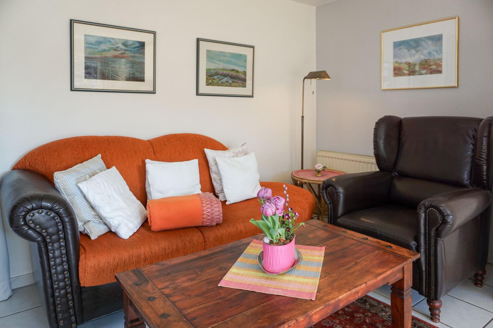 A living room with orange sofa, brown armchair, and wooden table with flowers.