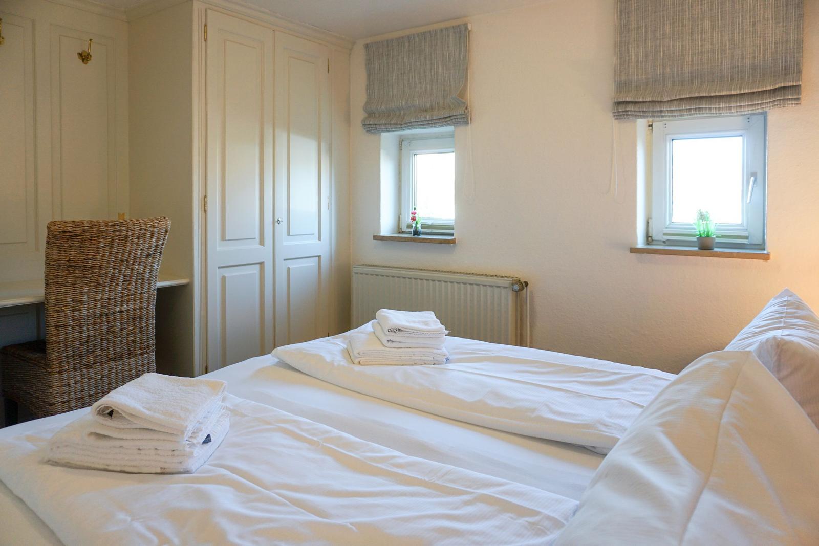Bedroom with bed, wardrobes, and windows with roller blinds.
