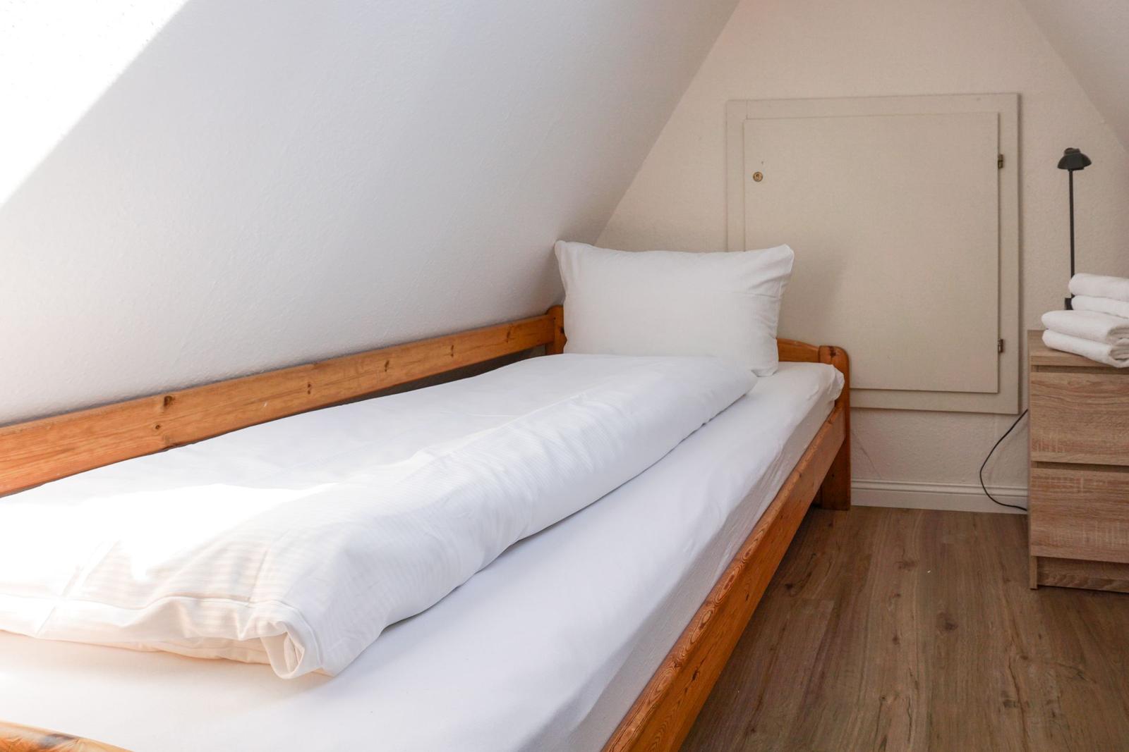A bed with white bedding and wooden frame under a sloped ceiling.