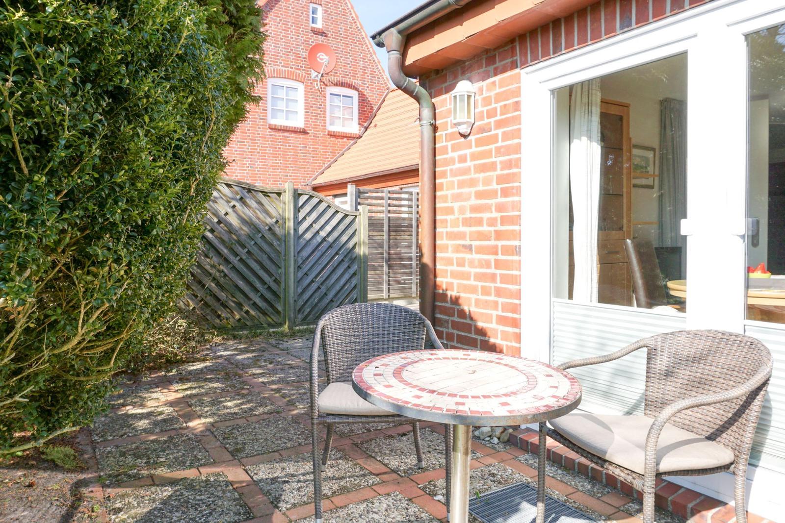 Terrace with table and two chairs in front of a house wall.