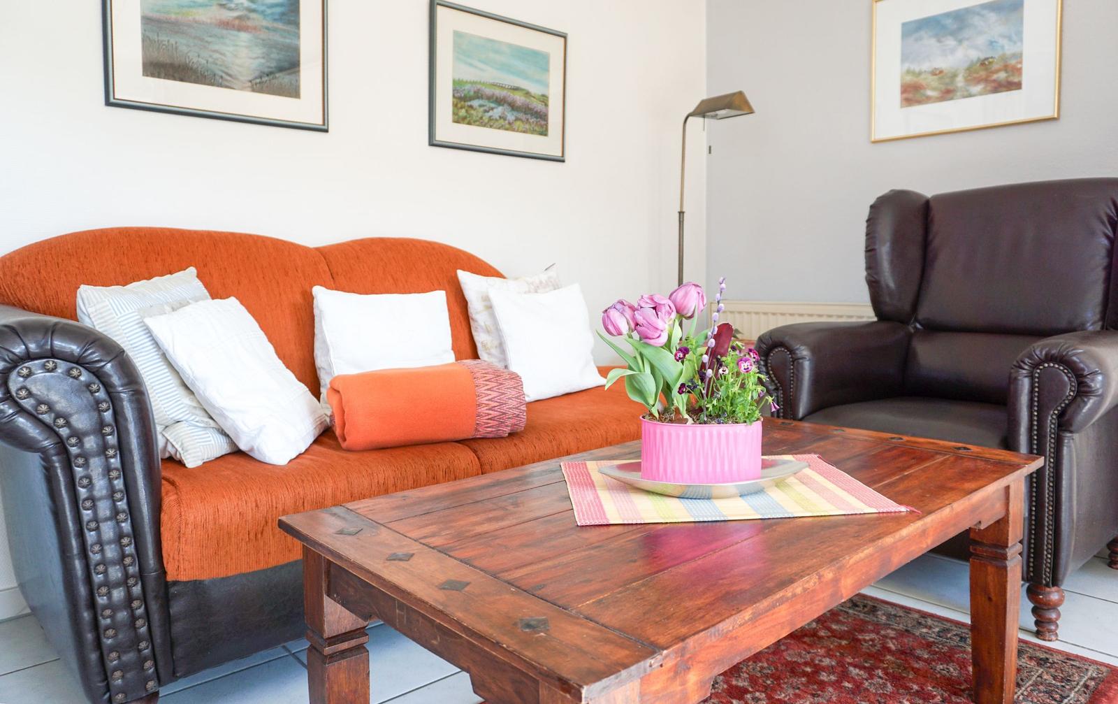 A living room with orange sofa, brown armchair, and wooden table with flowers.