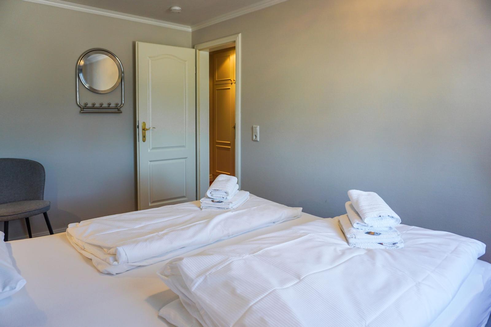 Room with bed, towels, chair, and mirror on the wall.