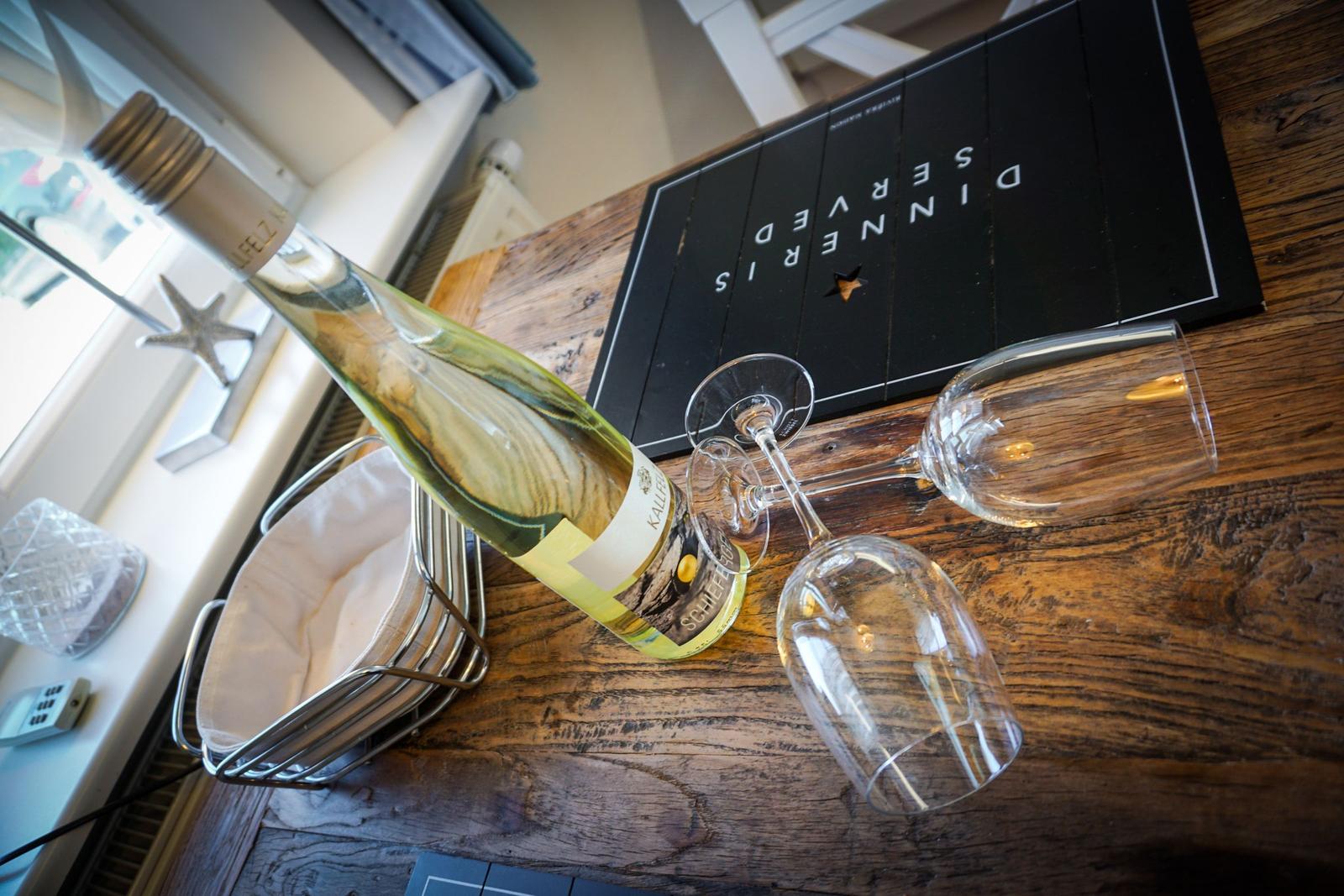 Wine bottle and two glasses on wooden table with dinner menu.