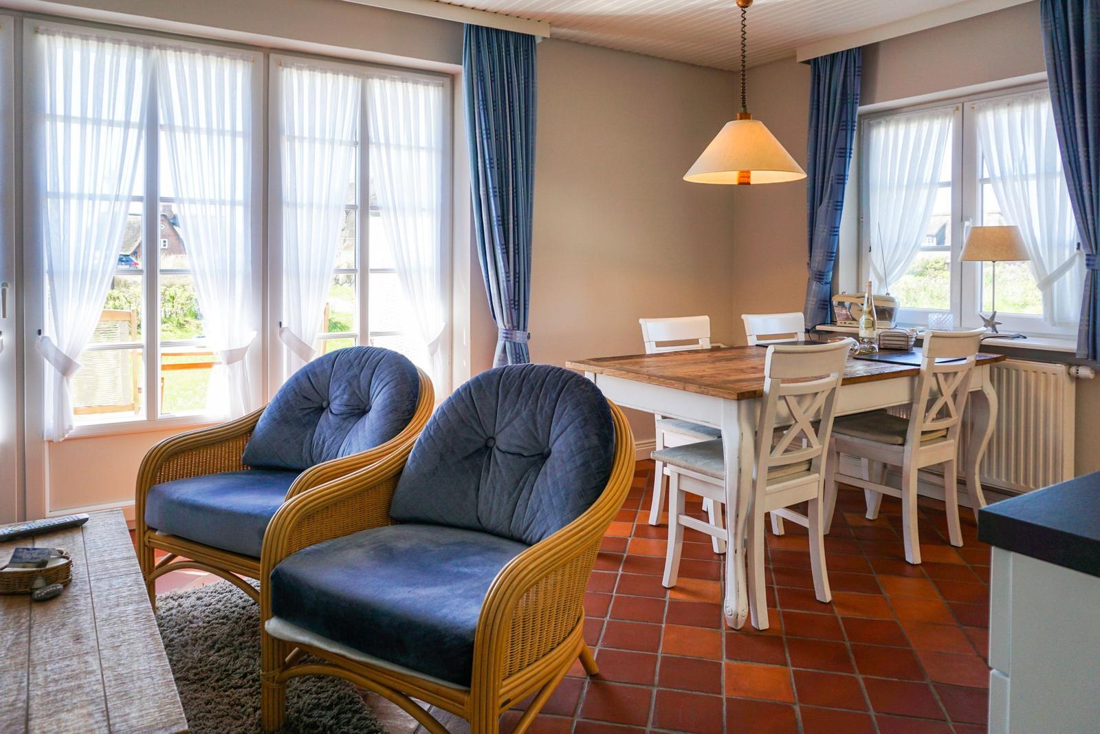 Two blue chairs and a dining table with chairs in the room with windows and terrace.