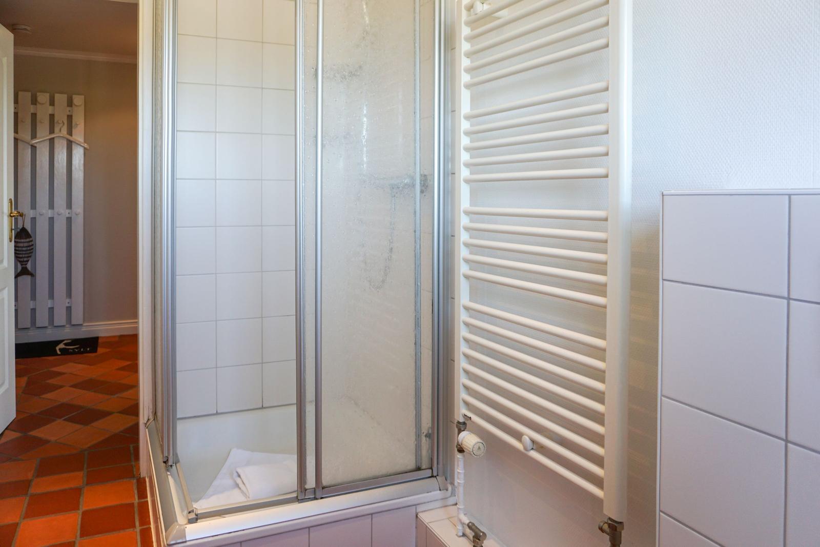 Shower with glass door, heater, and white tiles.