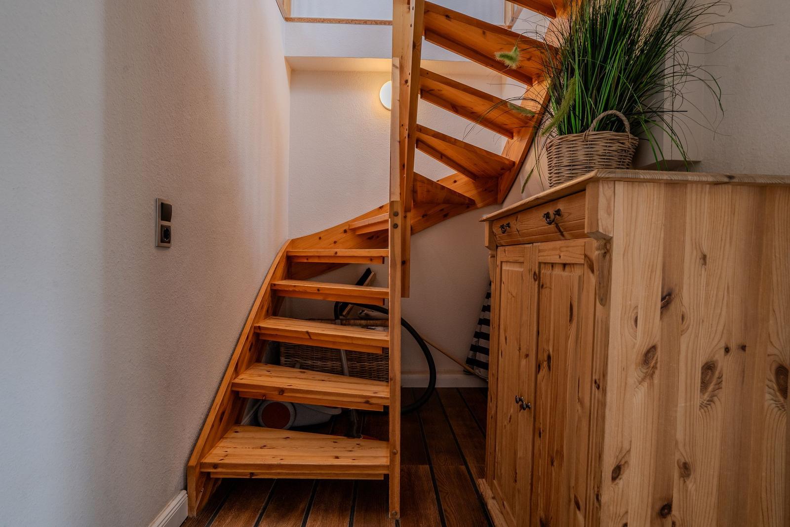 Holztreppe führt zur oberen Etage. Holzschrank und Pflanze im Vordergrund.