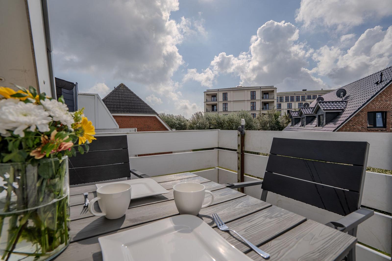 Terrasse mit Tisch, Stühlen und Blumen. Blick auf Gebäude und Himmel.