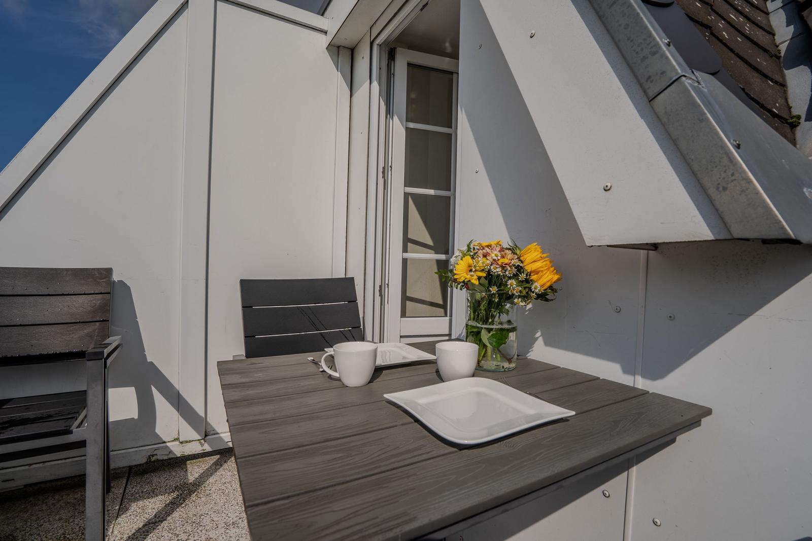 Terrasse mit Tisch, Stühlen und Blumenarrangement.