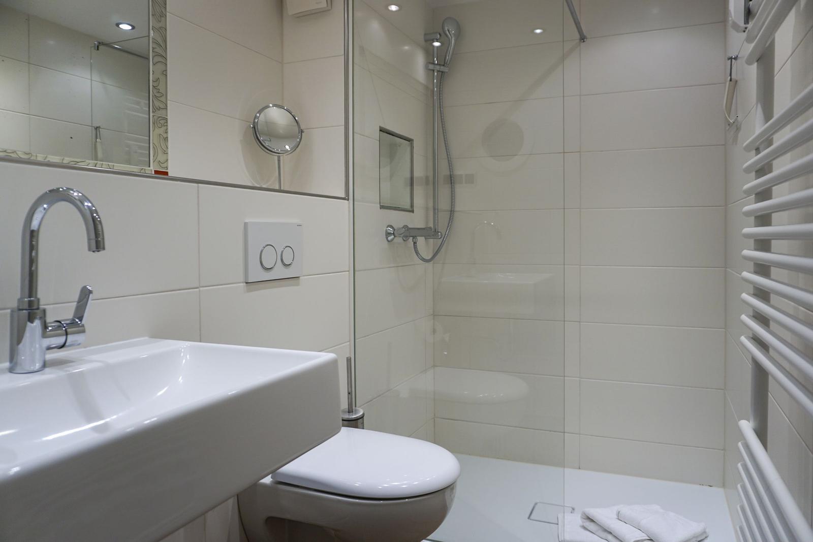 Badezimmer mit Dusche, Waschbecken und Toilette. Weiße Fliesen und moderne Armaturen.