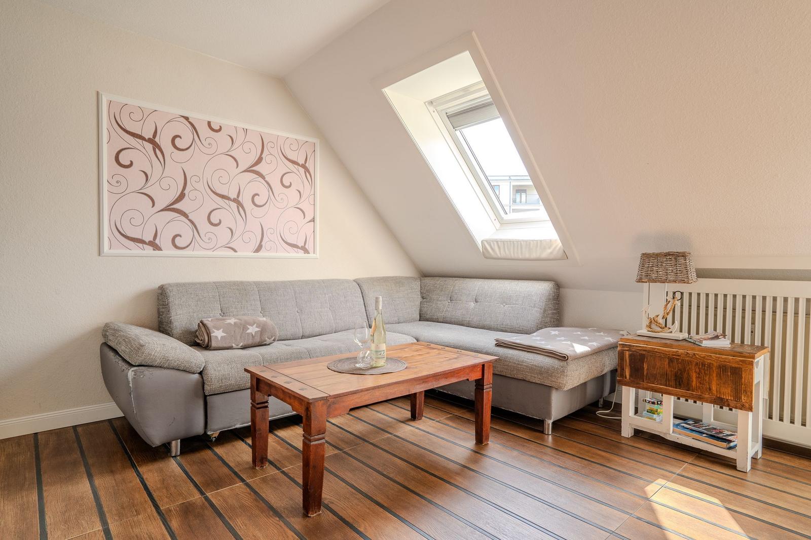Ein Wohnzimmer mit grauem Sofa, Holztisch und Dachfenster.