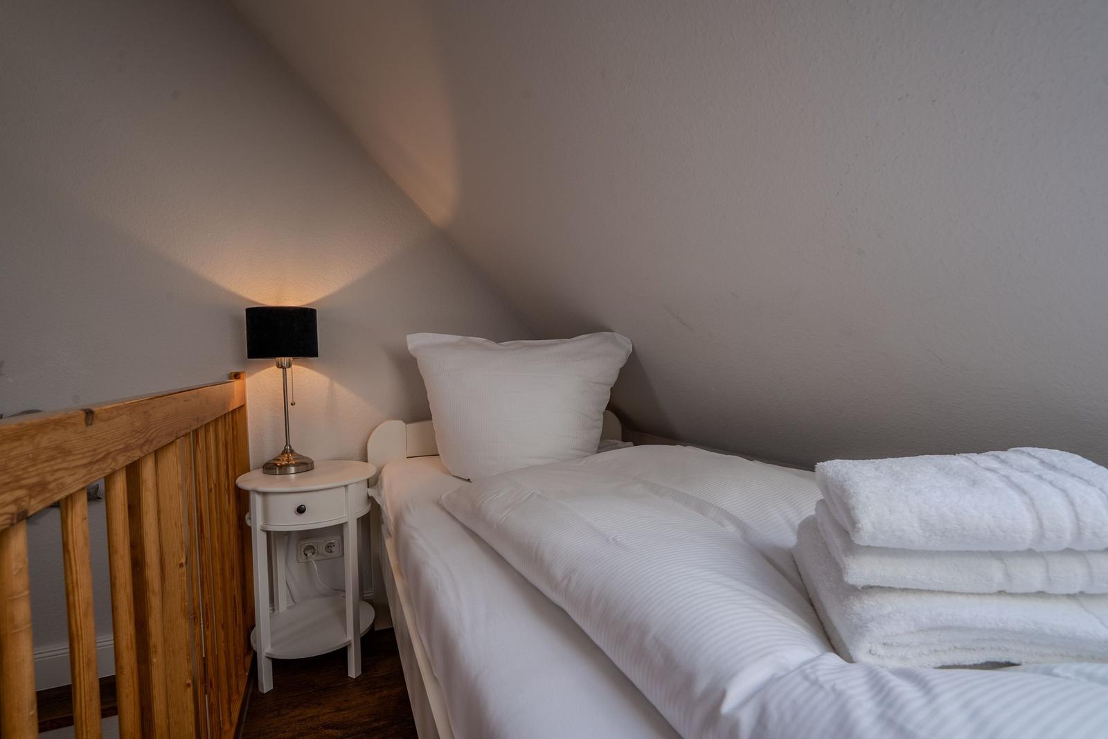 Ein Bett mit weißer Bettwäsche und Handtüchern. Neben dem Bett steht ein Nachttisch mit einer Lampe.