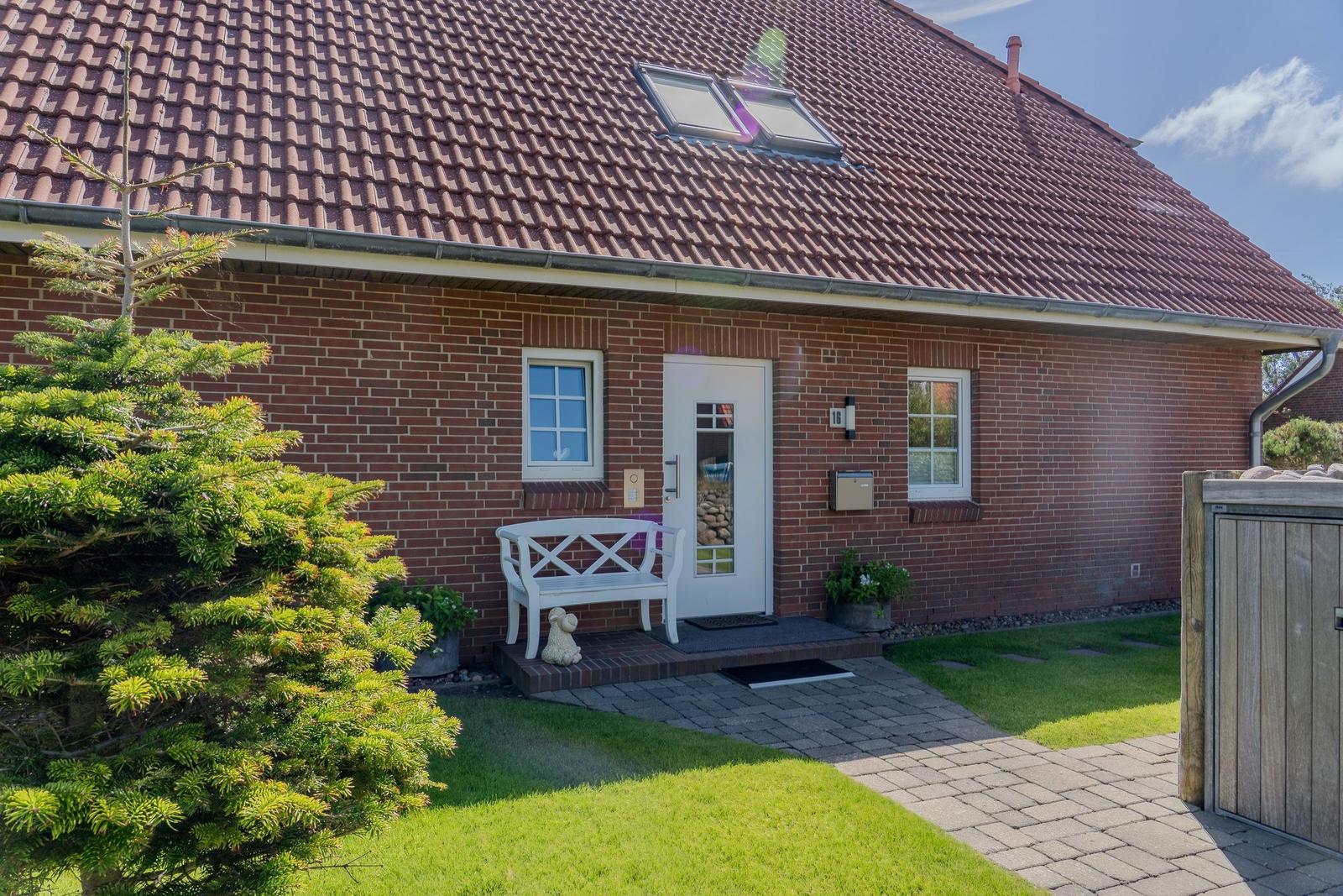 Haus mit rotem Ziegeldach, weiße Tür und Bank vor dem Eingang.