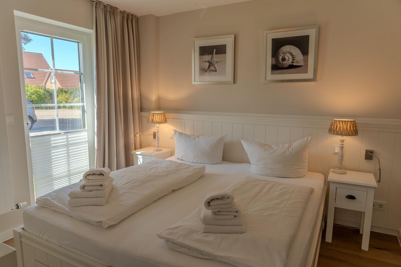 Schlafzimmer mit weißem Bett, Nachttischen und Fensterblick.