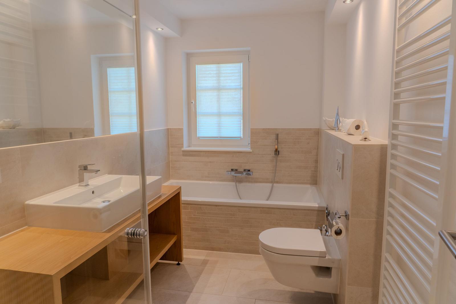 Badezimmer mit Badewanne, Toilette und Waschbecken auf Holzuntergestell.