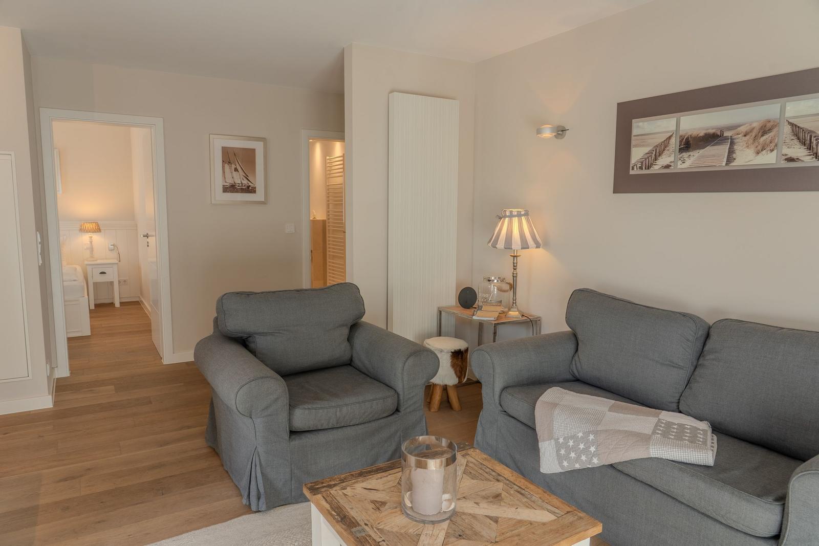 Wohnzimmer mit grauem Sofa und Sessel, Holzboden und Wandbild.