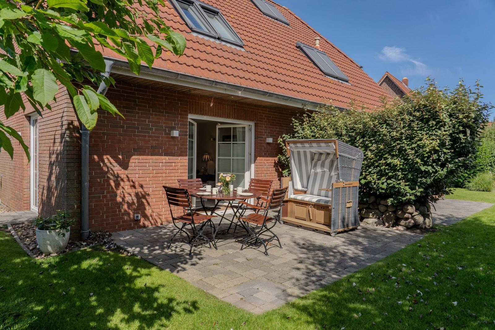Terrasse mit Tisch, Stühlen und Strandkorb vor rotem Backsteinhaus.