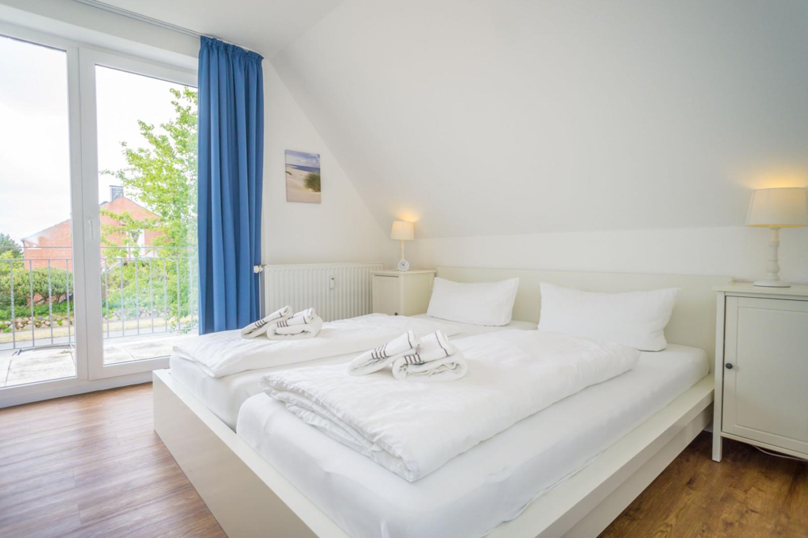 Schlafzimmer mit Doppelbett, Fenster und Holzboden.