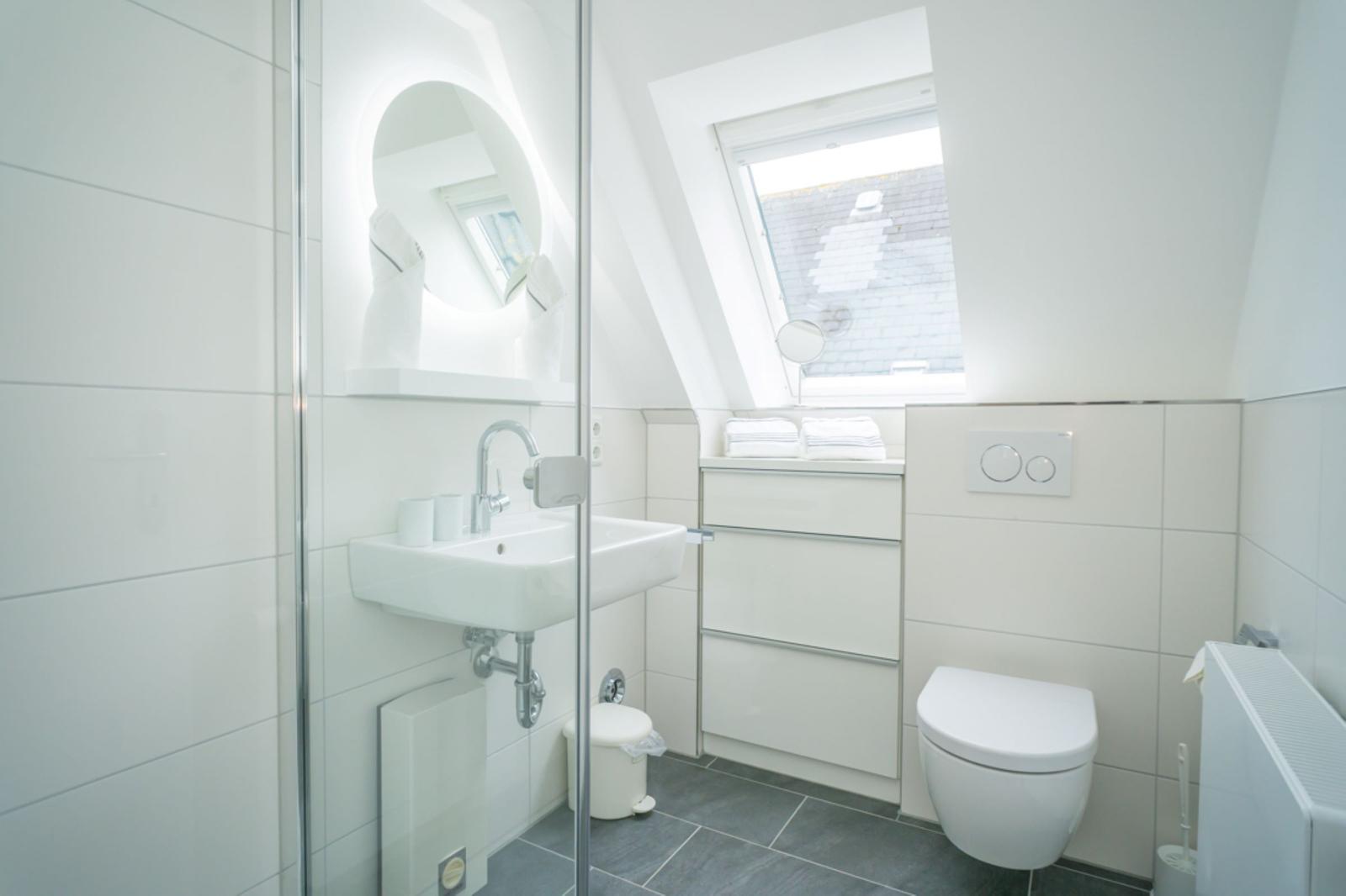 Badezimmer mit Dusche, Waschbecken und Toilette unter Dachschrägen.