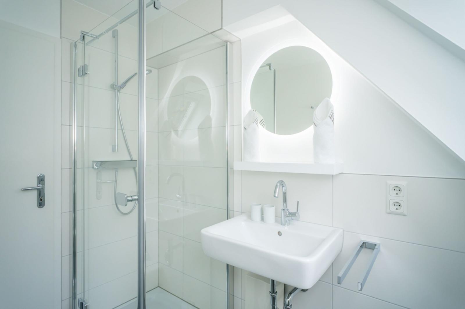 Badezimmer mit Dusche, Waschbecken und runden Spiegel