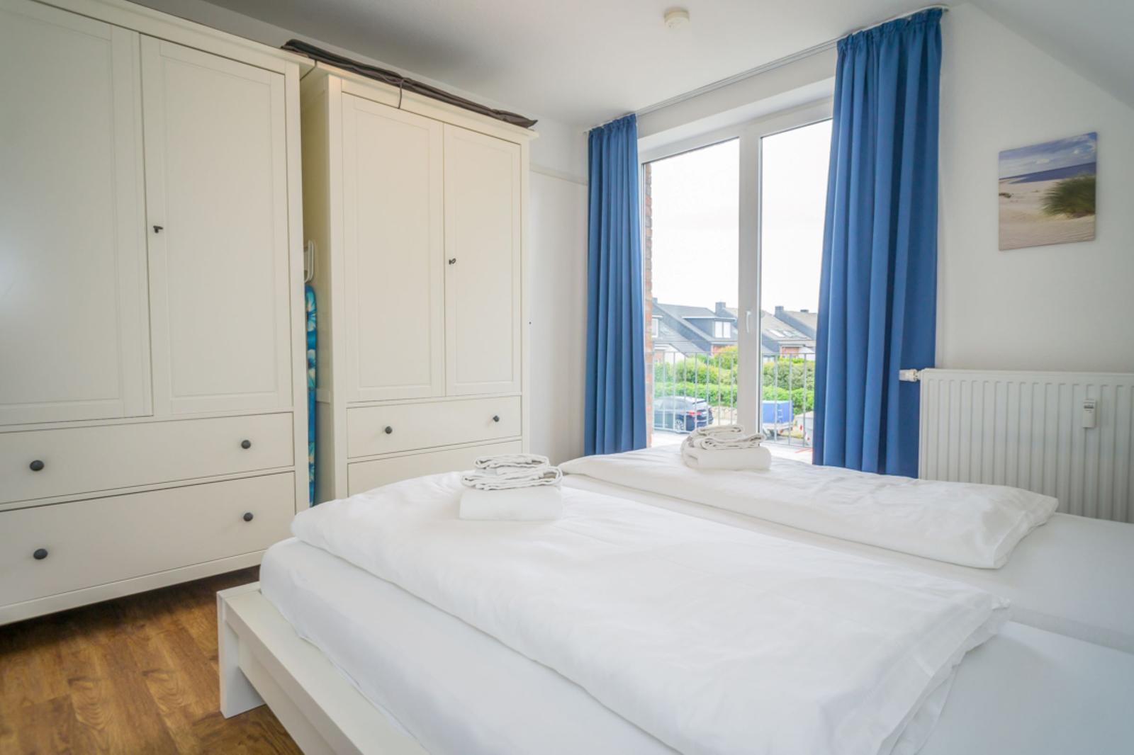 Zimmer mit Doppelbett, weißen Schränken und blauen Vorhängen vor Fenster