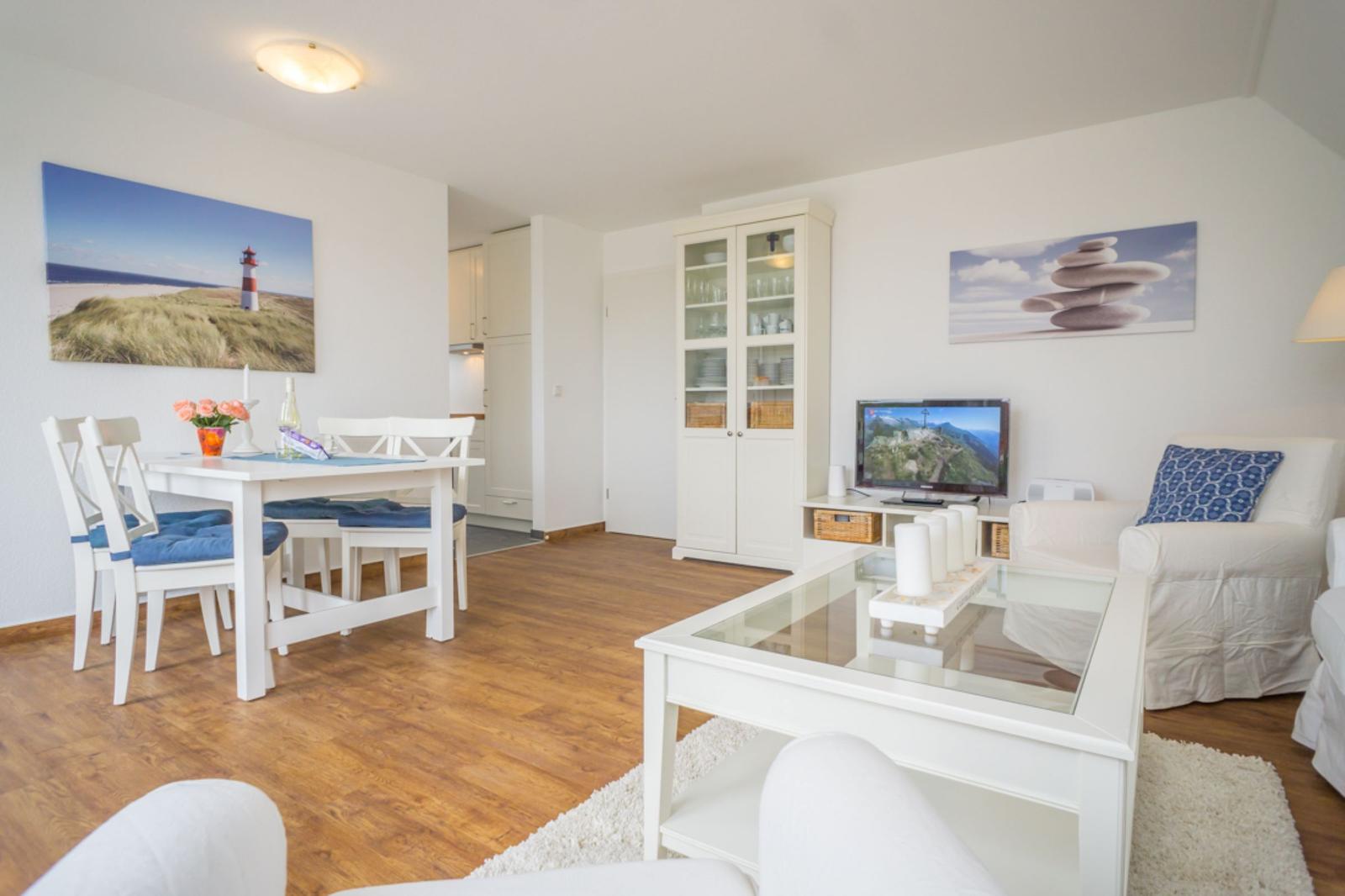 Wohnzimmer mit Esstisch, Fernseher und Glas-Tisch. Hölzerner Boden und weiße Möbel.