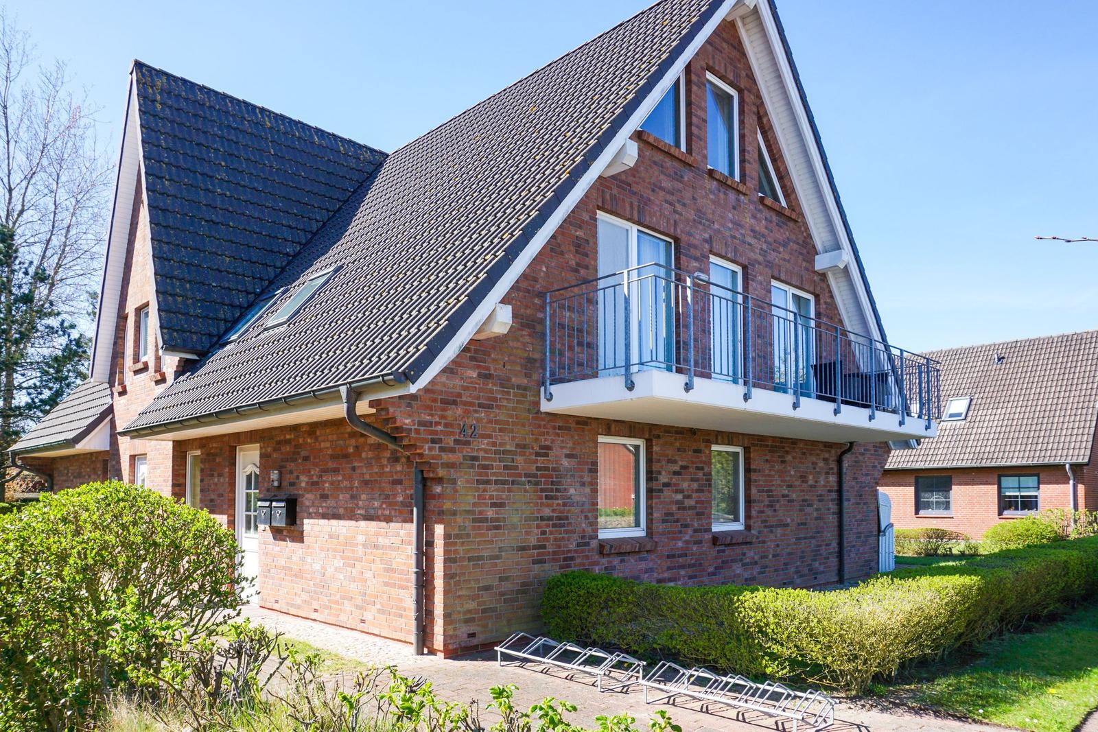 Zweistöckiges Haus mit Balkon und Dachfenstern, umgeben von Grünflächen.