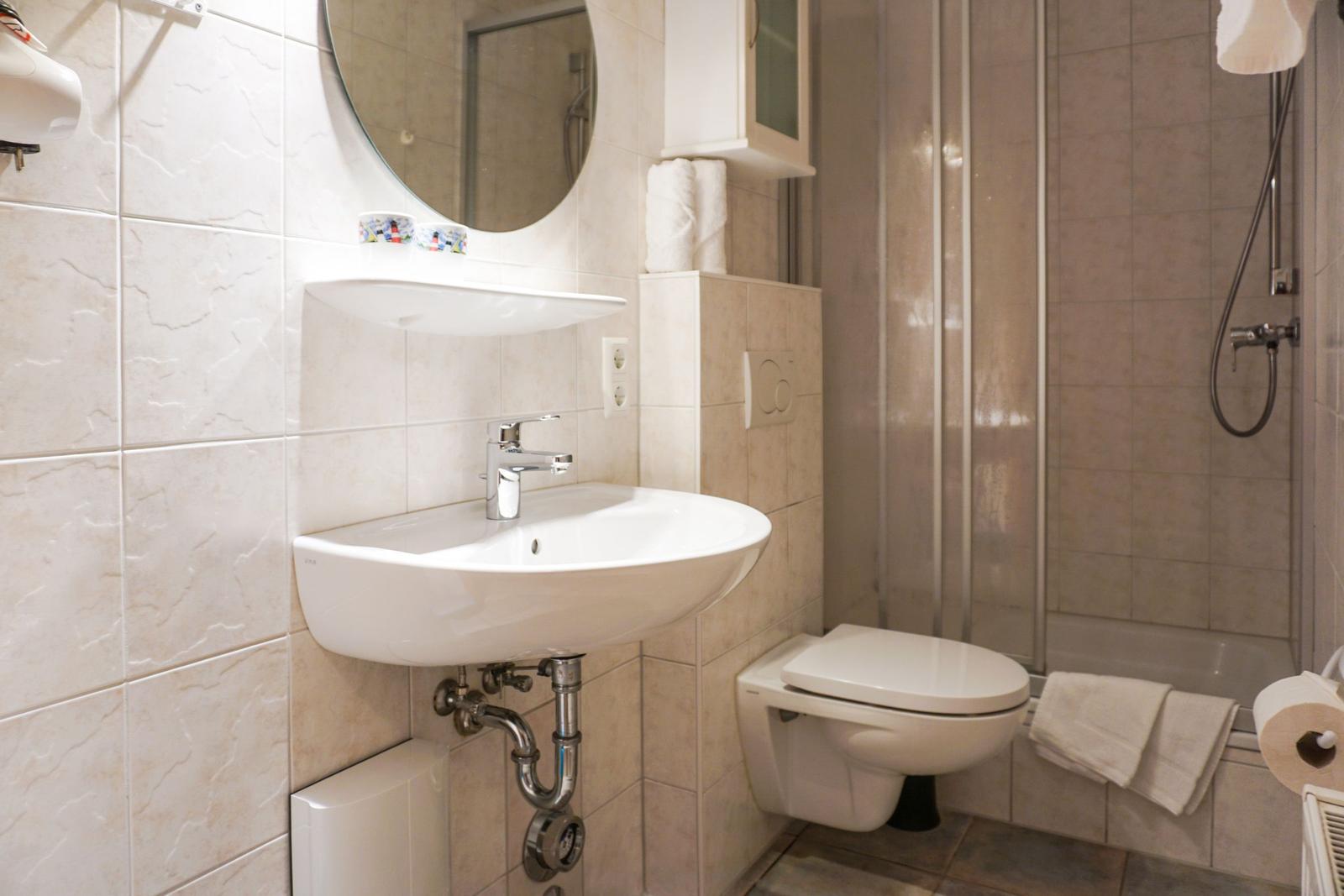 Badezimmer mit Waschbecken, Spiegel, Toilette und Dusche.