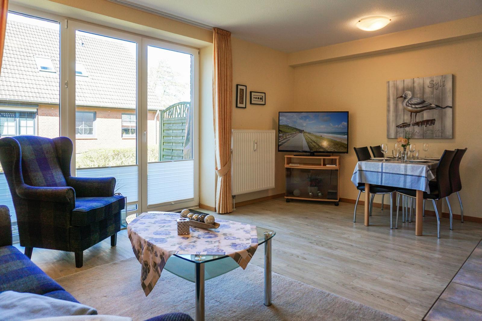 Wohn- und Essbereich mit TV, Tisch und Stühlen, großes Fenster und Wandbild mit Möwe.
