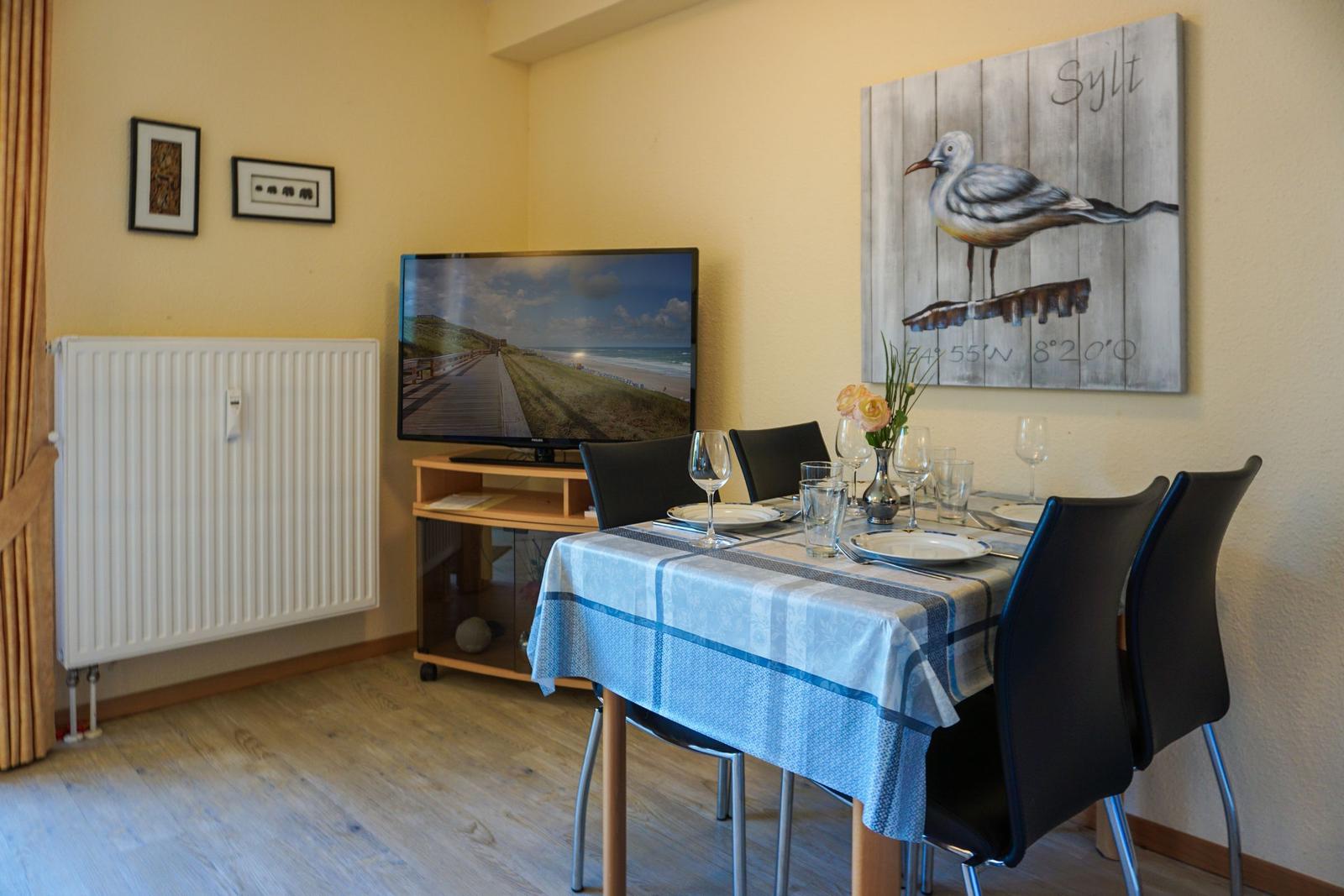 Essbereich mit Tisch, Stühlen und Fernseher an der Wand.
