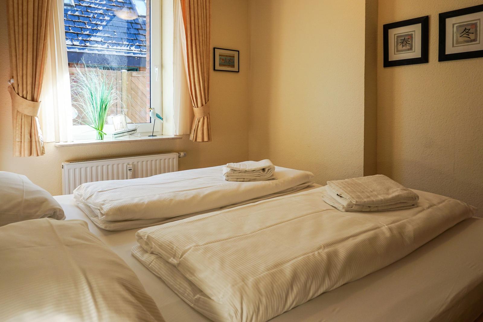 Zimmer mit zwei Betten, Fenster mit Vorhängen und Wandbildern.