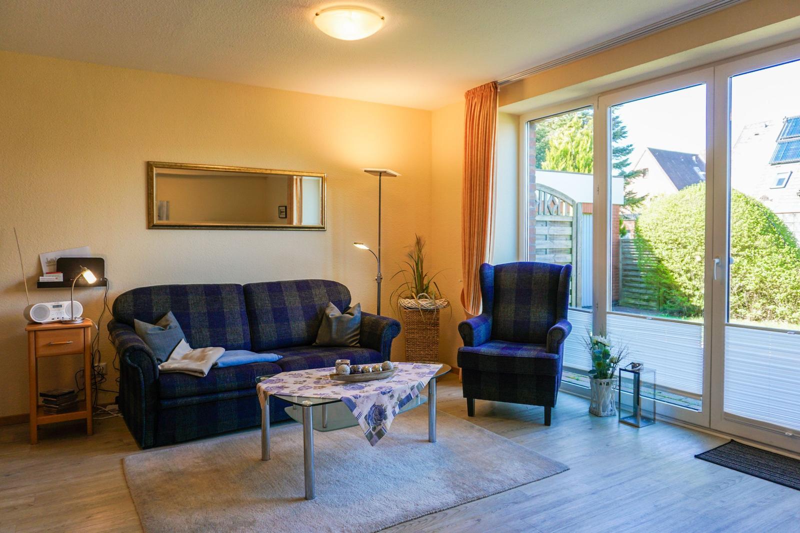 Wohnzimmer mit Sofa, Sessel und Glastür zur Terrasse.