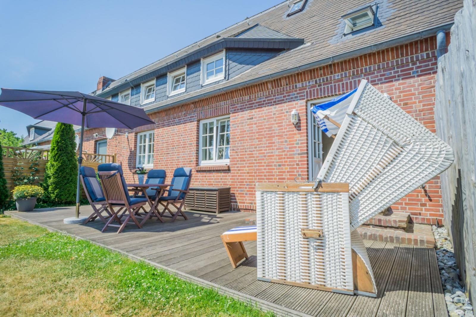 Terrasse mit Tisch, Stühlen und Sonnenschirm. Weiße Strandkörbe stehen auf der Terrasse.