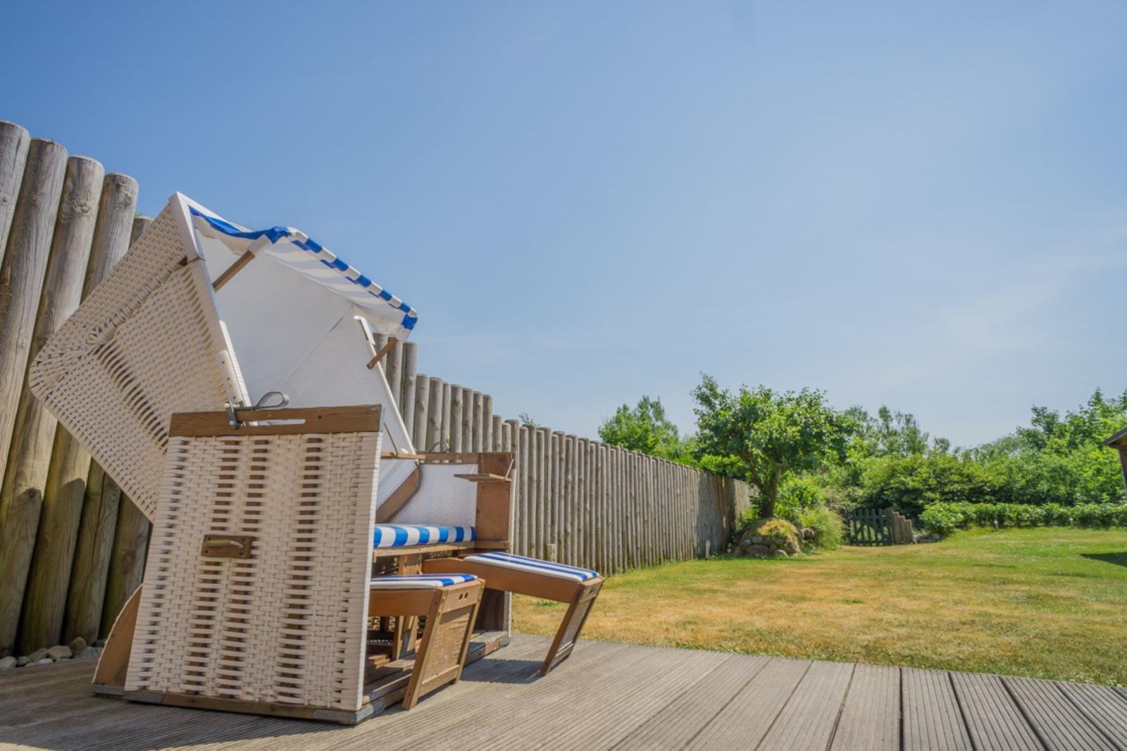 Hochwertige Strandkörbe auf Holzterrasse mit Blick auf Grünfläche und Holzzaun.